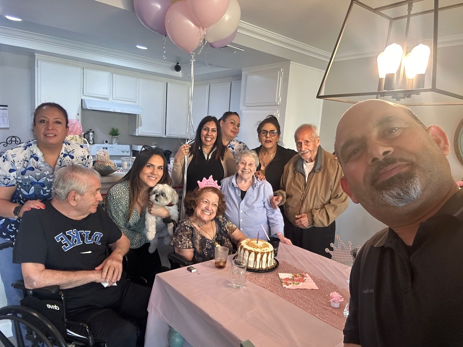 A group of people celebrating a birthday around a table with balloons.