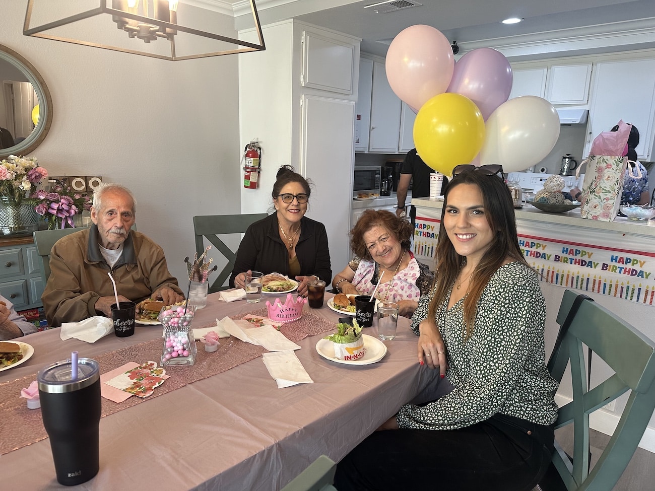 A family celebrates a birthday with food and colorful balloons in a decorated dining room.