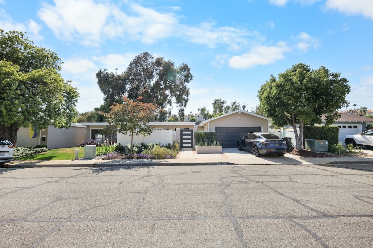 Modern suburban house with a car in the driveway, surrounded by trees and a clear sky.