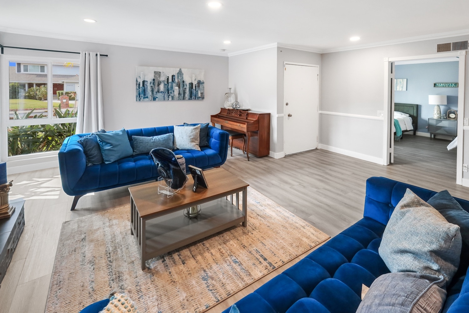Modern living room with blue sofas, artwork, and a piano. Cozy ambiance with natural lighting and contemporary decor.