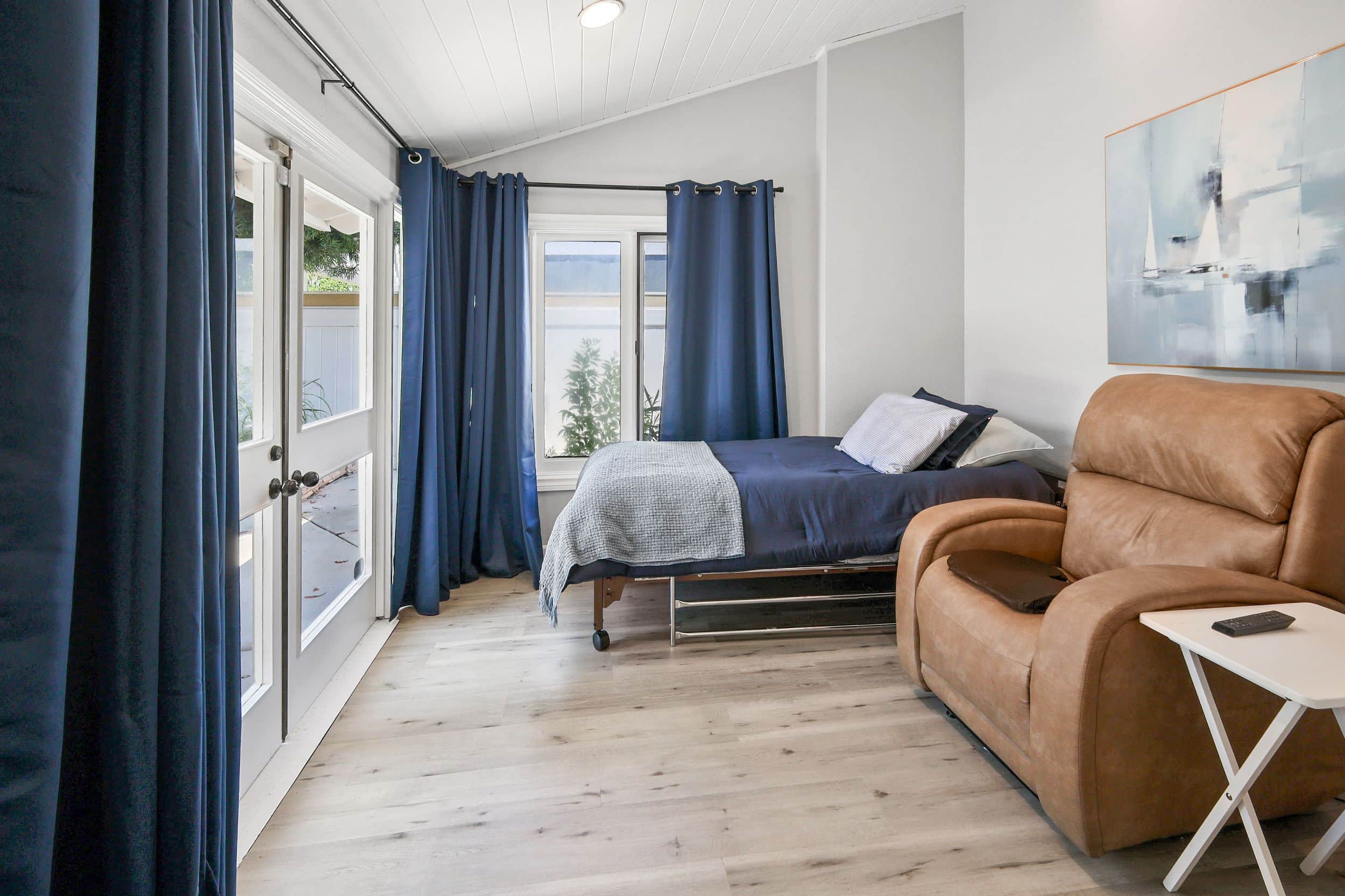 Modern bedroom with blue curtains, bed, recliner, and side table.