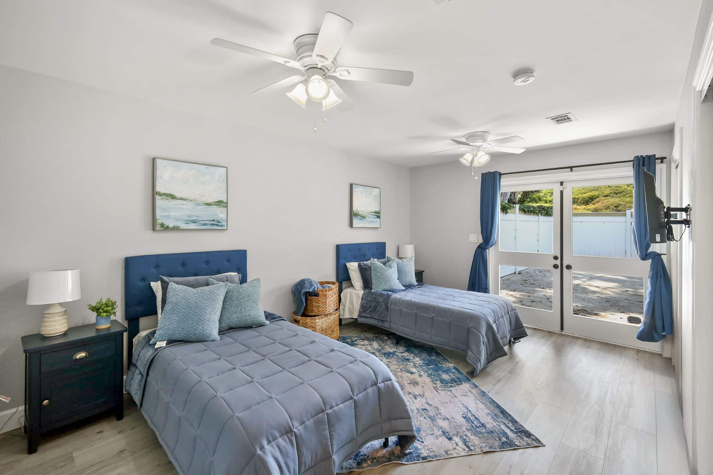 Bedroom with two twin beds, navy accents, blue pillows, large window, and modern decor.