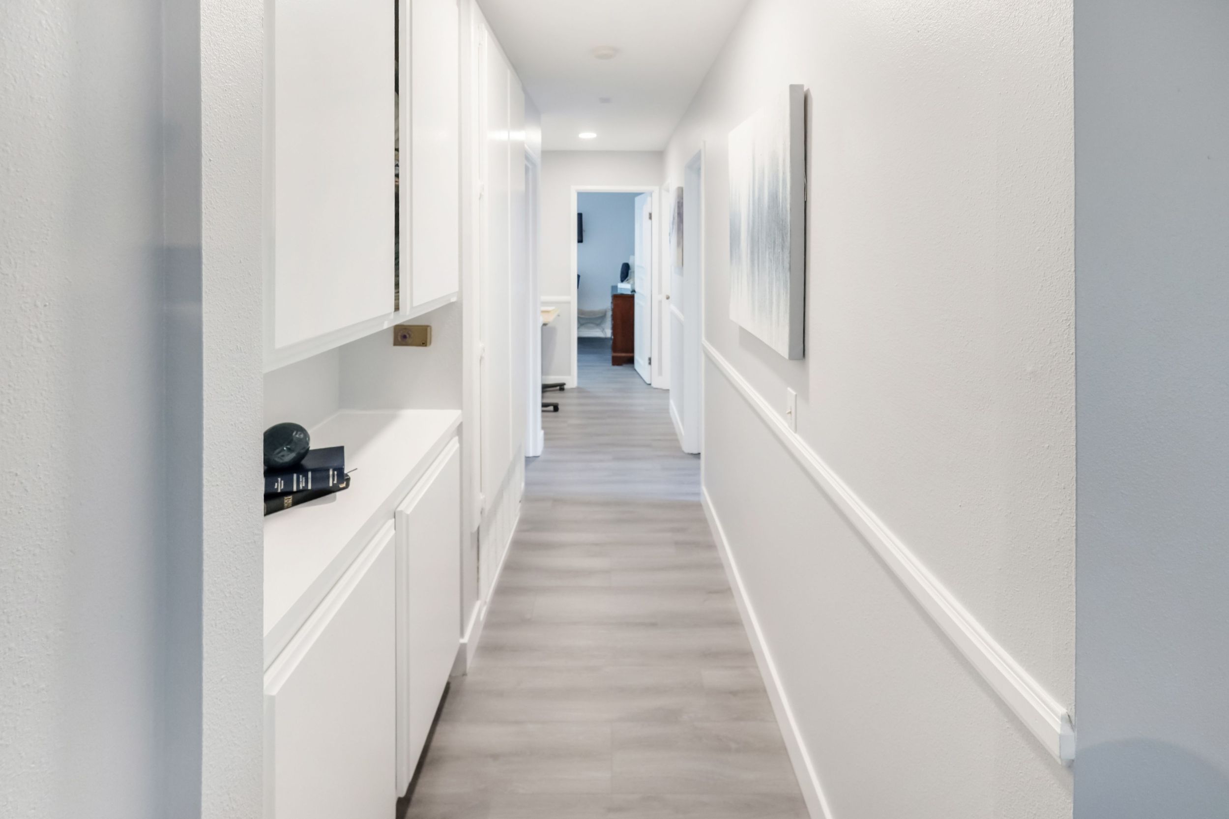 Bright hallway with white cabinets and a painting on the wall.