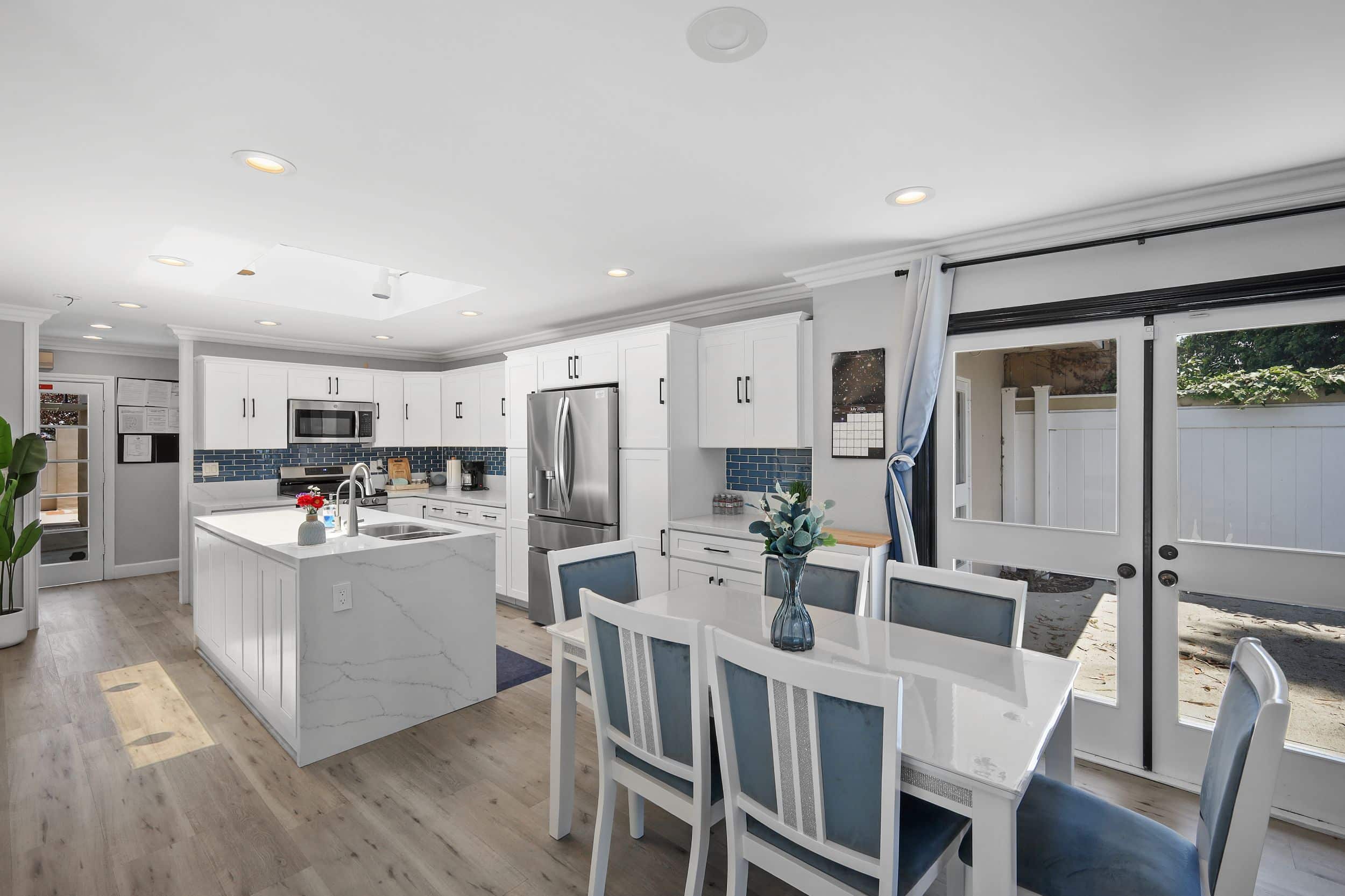 Modern kitchen with white cabinets, island, stainless steel appliances, and dining table with blue chairs.