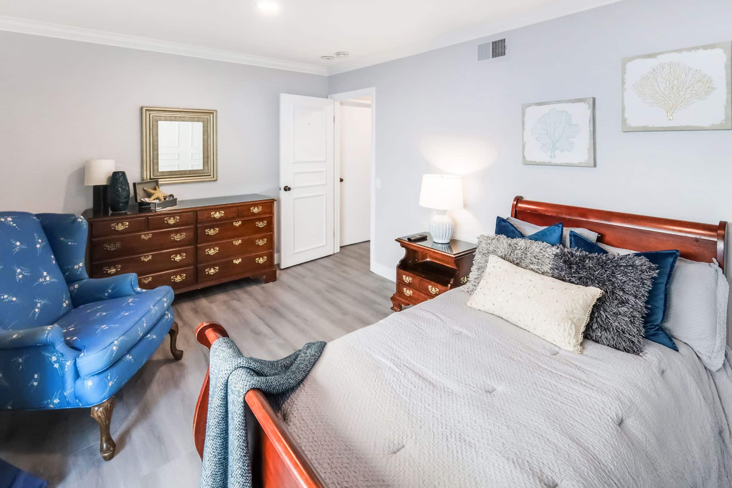Cozy bedroom with wooden furniture, blue armchair, and decorative pillows on a neatly made bed.