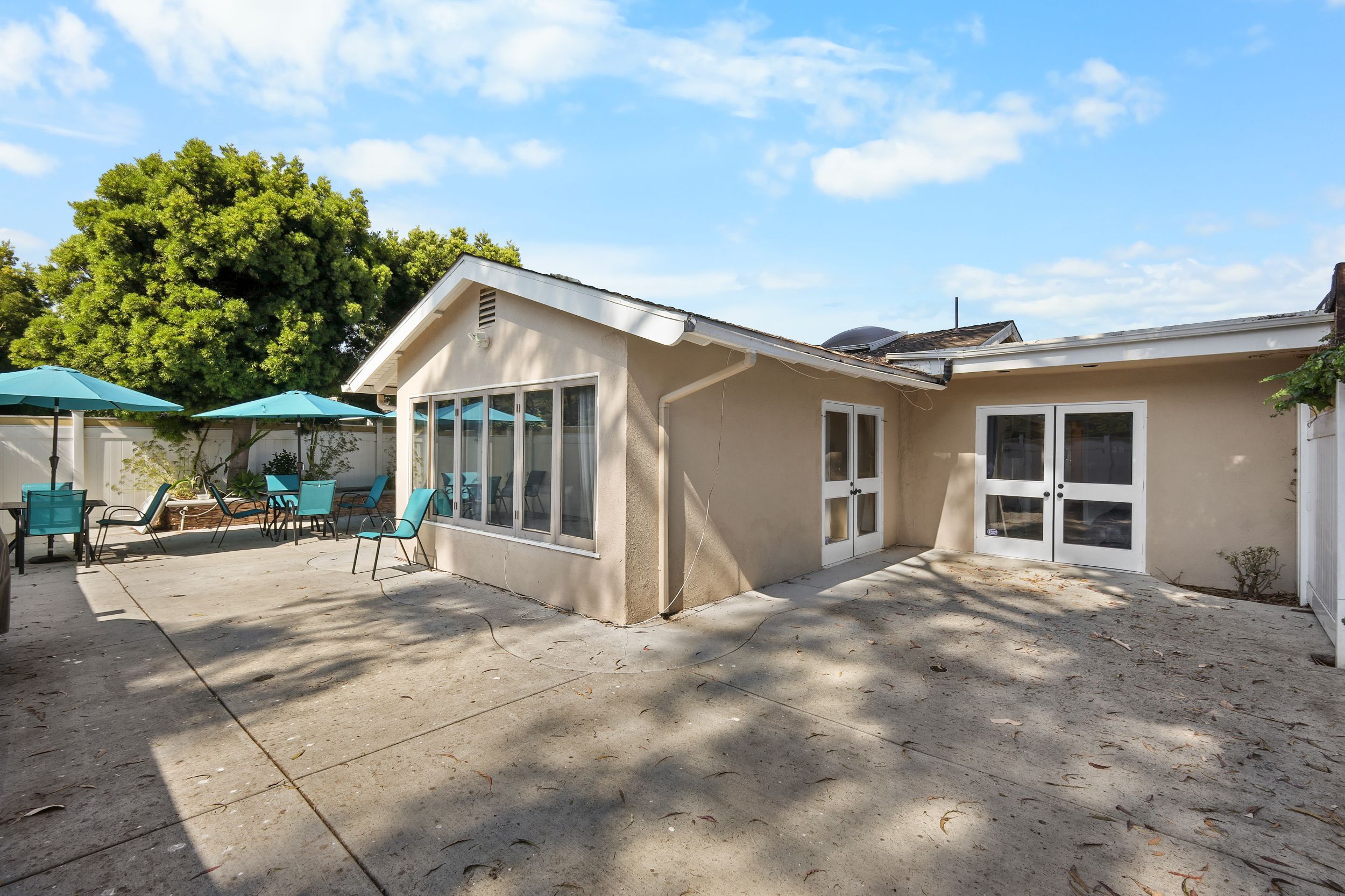 Outdoor patio with teal chairs and umbrellas, adjacent to a beige house under a blue sky.