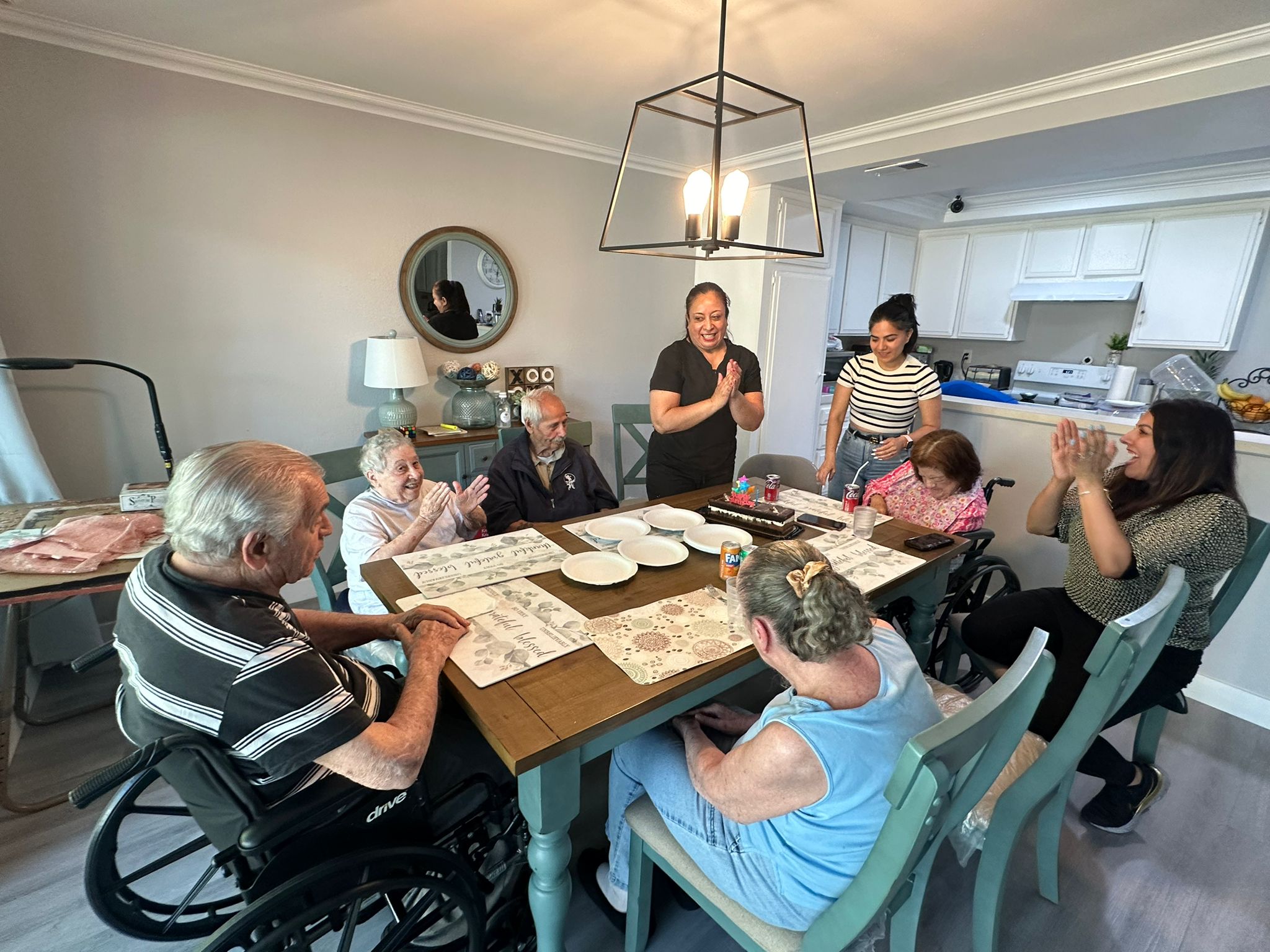 Group of people clapping and engaging in a social activity around a dining table in a cozy setting.