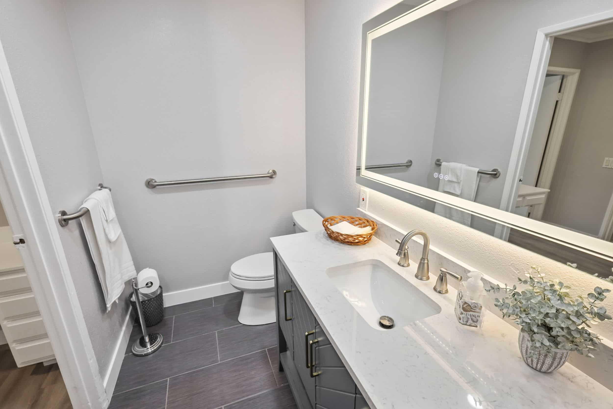 Modern bathroom with gray tiles, wall-mounted sink, and large mirror.