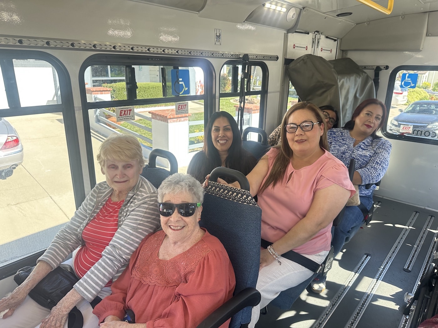 Group of women seated inside a bus, smiling at the camera.
