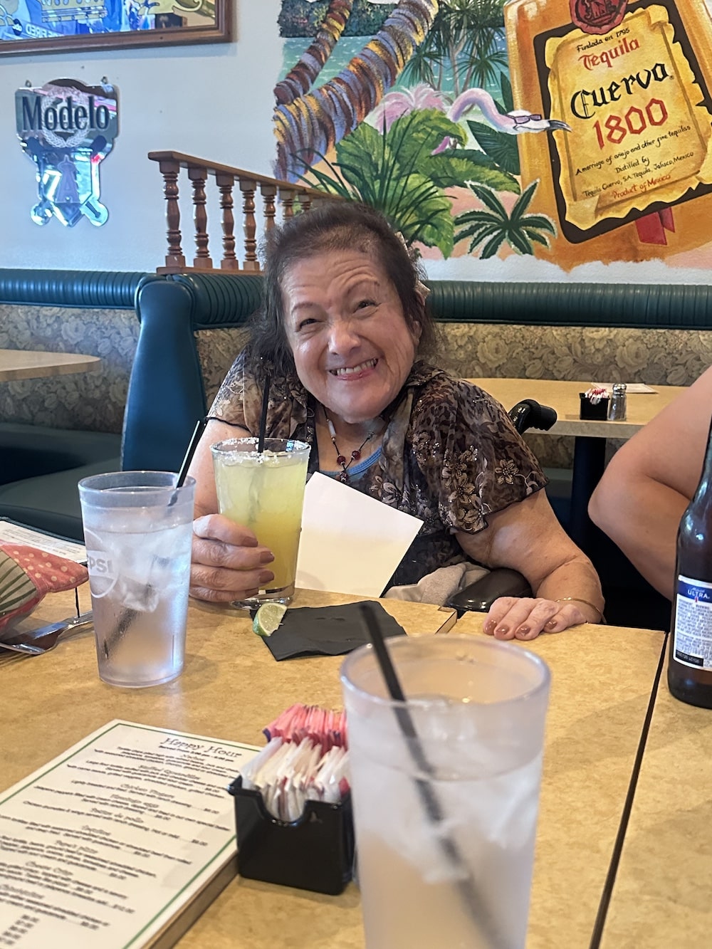 A woman smiling while holding a margarita in a restaurant setting.