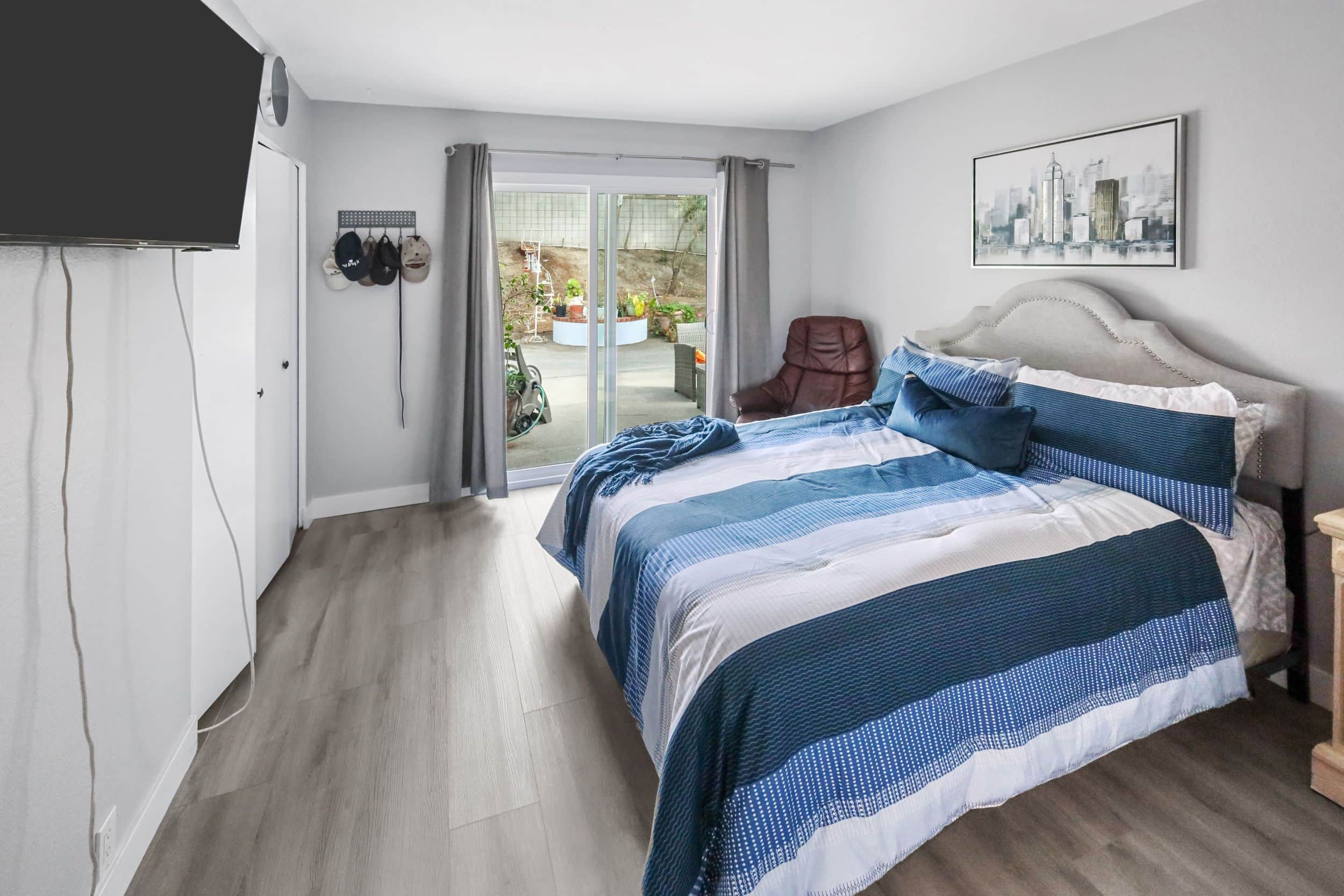 Modern bedroom with blue bedding, wall art, sliding glass door, and TV.