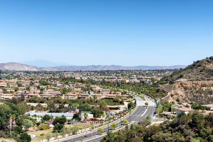 Aerial view of a suburban neighborhood with winding roads and scenic hills under a clear blue sky.