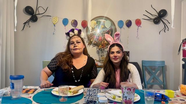 Two women in costume sitting at a table with party decorations and food.