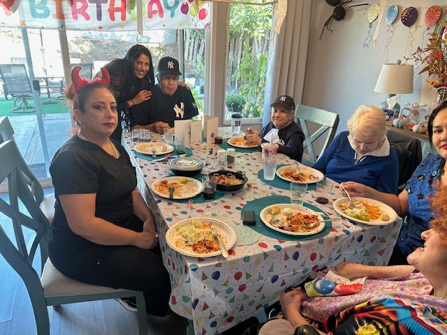 A group of people sitting around a table having a meal, with birthday decorations in the background.